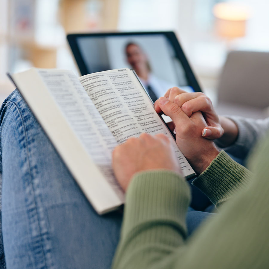 Aufgeschlagene Bibel vor einem Tablet mit Videokonferenz