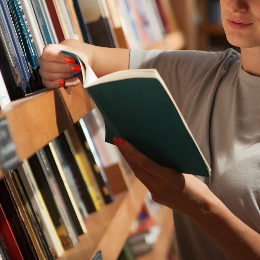 Hand greift ein Buch aus einem Bücherregal